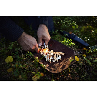 The brown leather pad is picrured on the woodland floor, with shavings being lit on fire on top of it, to keep them dry before moving to the fireplace.