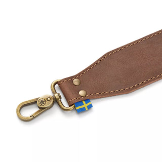 Hults Bruk Leather Axe Sling - a brown leather sling with brass fittings bearing the HB logo, and a Swedish Flag label