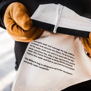 The Forest Fundamentals Millbbank Bag, a Black and white water filter bag, with instructions shown, held by gloved hands.