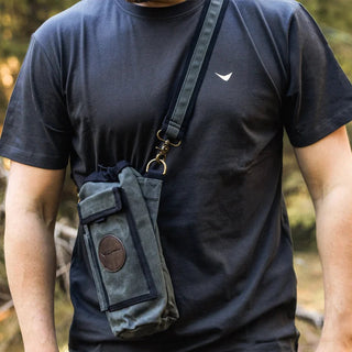A green waxed canvas water bottle pouch, with extra pockets for other items, featuring a shoulder strap, shown here across a model's body.