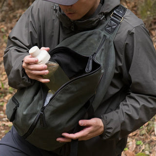 The DD Crosswind Sling bag, shown here diagonally across the front of a person's body, while they retrieve a water bottle.