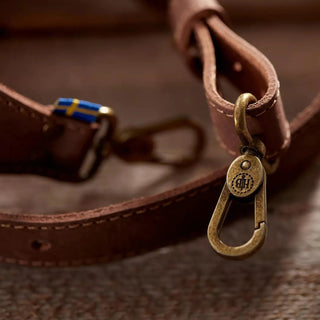 Brown leather axe sling with brass clasps and a Swedish flag label.