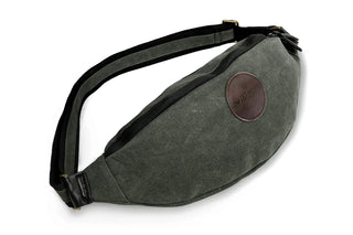 A Green waxed canvas pouch designed to be worn diagonally across the body. Brown leather logo patch, and a zipped top to keep contents secure.