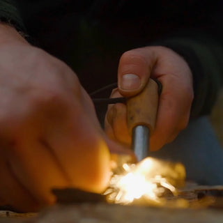 Forest Fundamentals Artisan fire lighter ferrocerium rod. Featuring a piece of Fatwood, a ferro rod, and a striker, tied together with paracord, showing a shower of sparks.