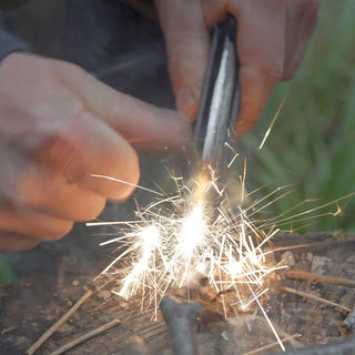 Forest Fundamentals Stealth Firelighter, a ferrocerium rod, in an aluminium holder, with fire lighting cord, striker, and lanyard. A shower of hot sparks.