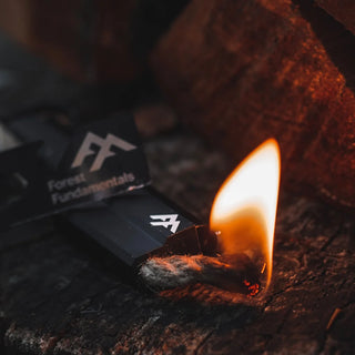 Forest Fundamentals Stealth Firelighter, a ferrocerium rod, in an aluminium holder, with fire lighting cord, striker, and lanyard. The fire cord is lit showing a small candle like flame.