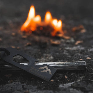 Forest Fundamentals Hive fire lighting Ferrocerium rod. These are hexagonal fire steels, and are supplied with a steel scraper, paracord and a carabiner. Shown here with the coating scraped off and a lit fire behind.